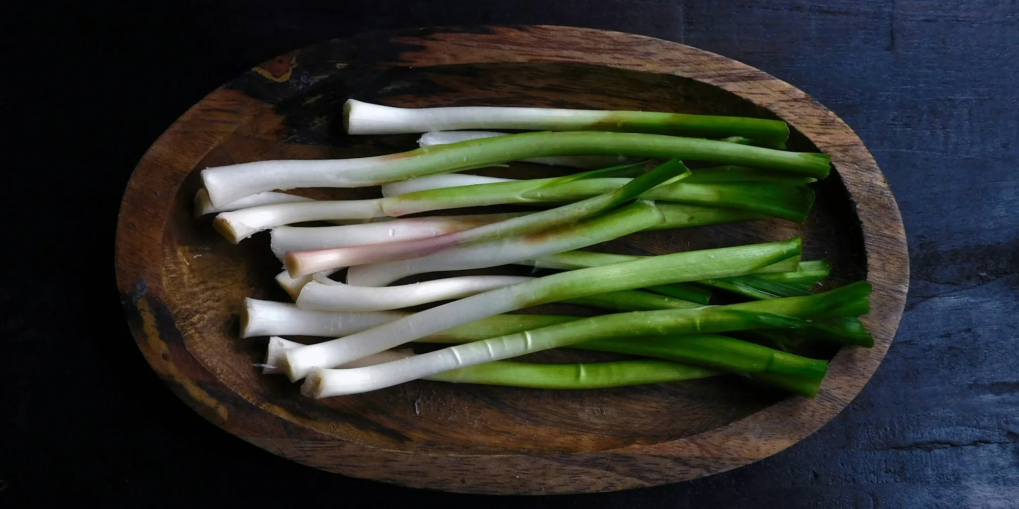 A wooden bowl of trimmed scallions