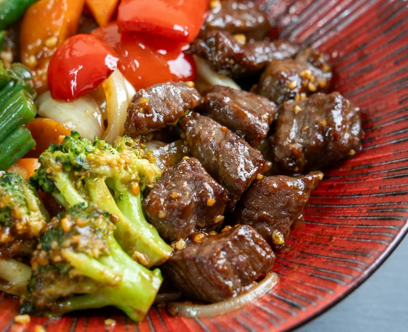 Beef and broccoli stir-fry with vegetables on a red plate