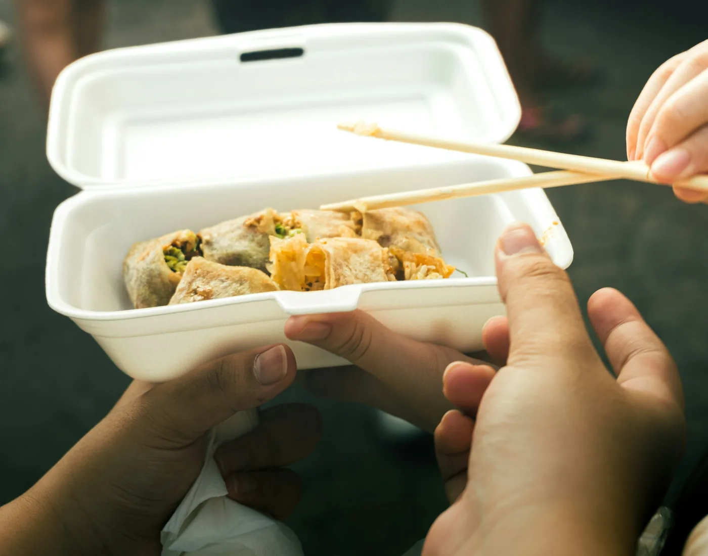 A takeout container of Chinese food held with chopsticks