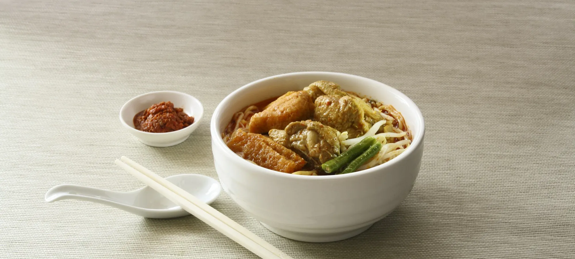 A bowl of cooked noodles beside chopsticks