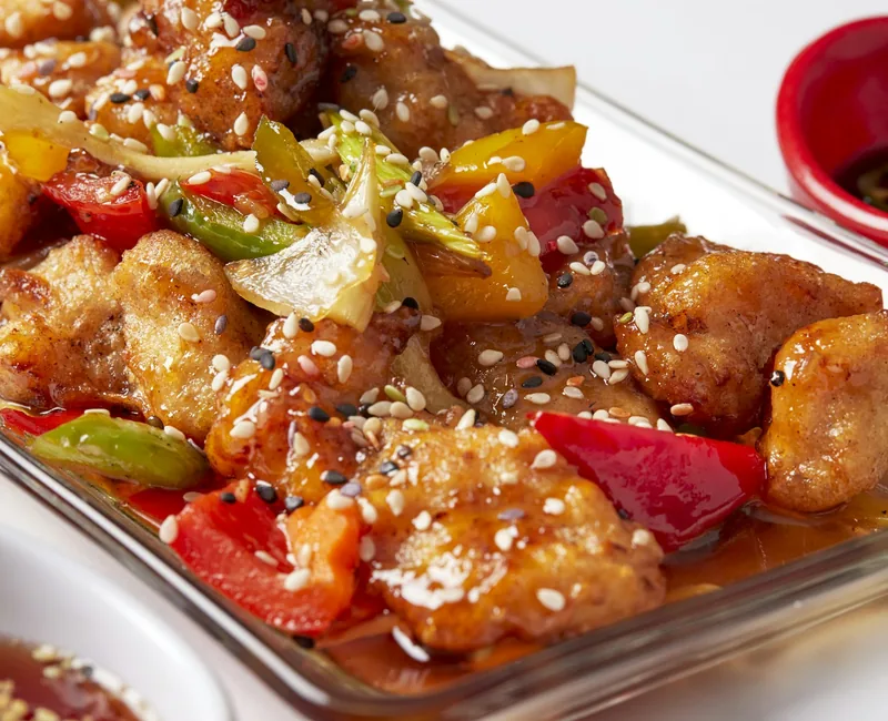 Golden sesame-glazed chicken plated on white ceramic
