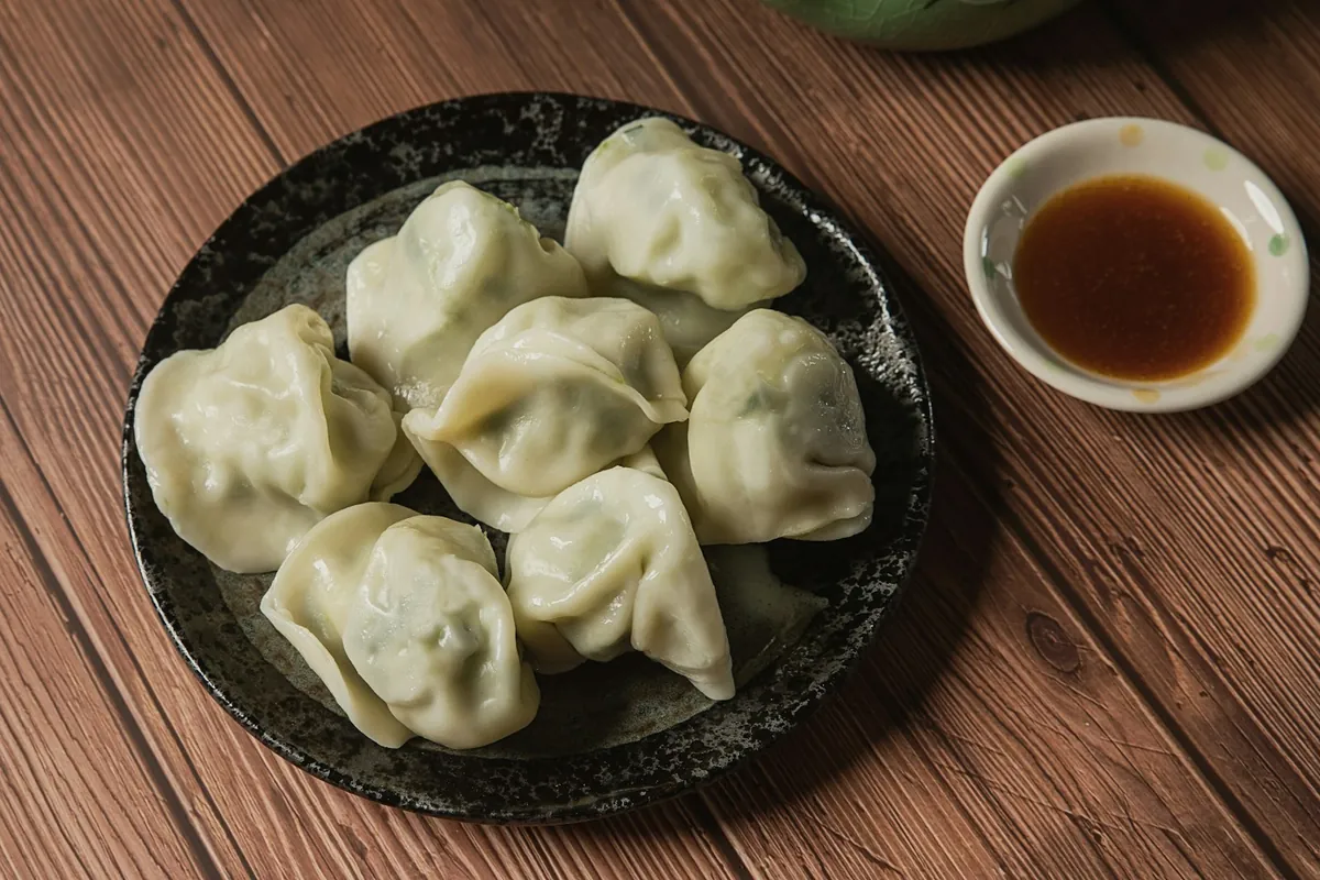 Dumplings beside a dish of dark dipping vinegar