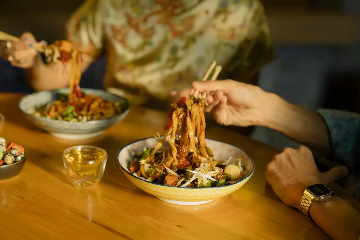 Long noodles lifted from a bowl with chopsticks