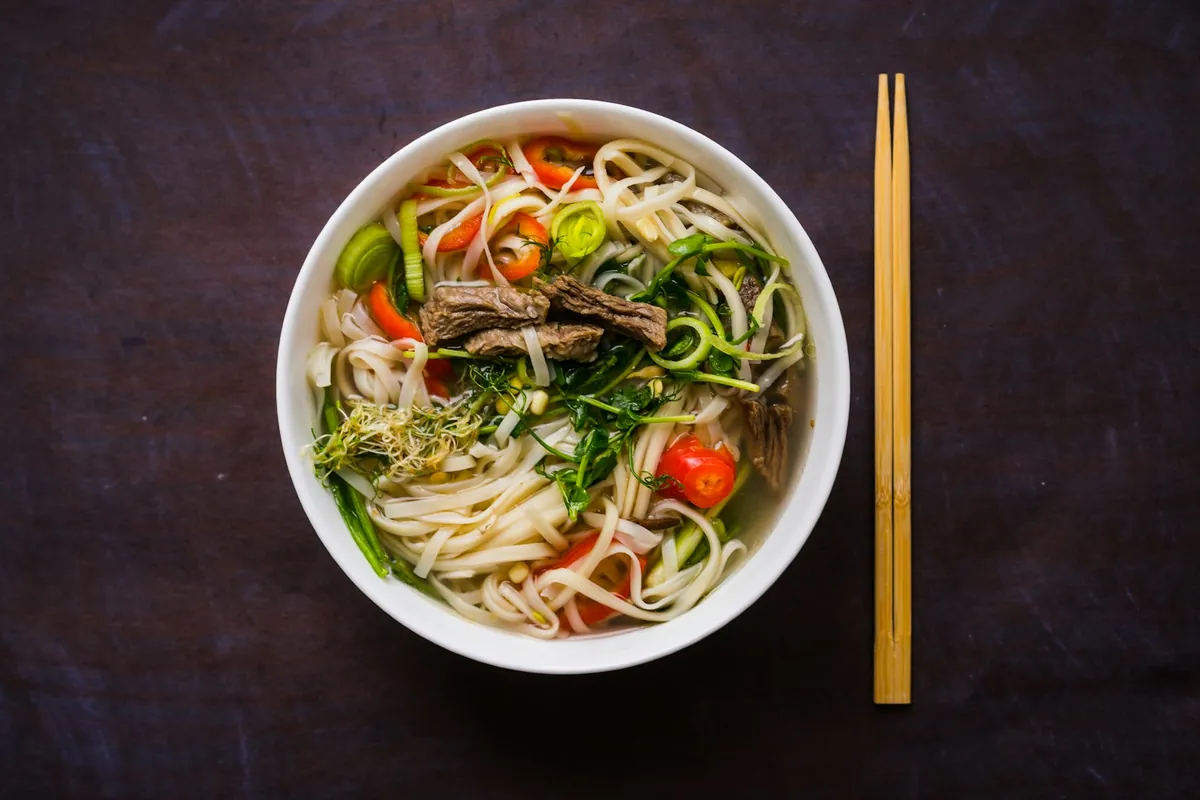 A bowl of Chinese noodles with chopsticks resting on the rim